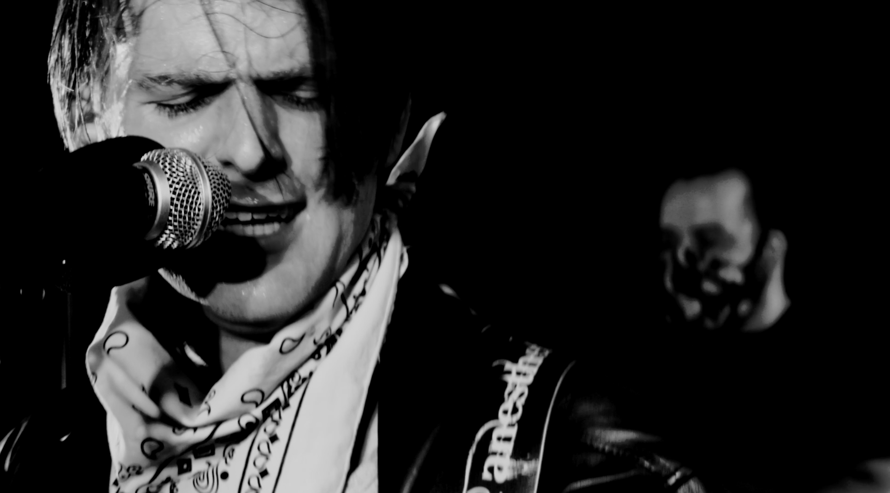 Black and white cinematic portrait of male singer in dramatic studio lighting man wearing face mask behind him