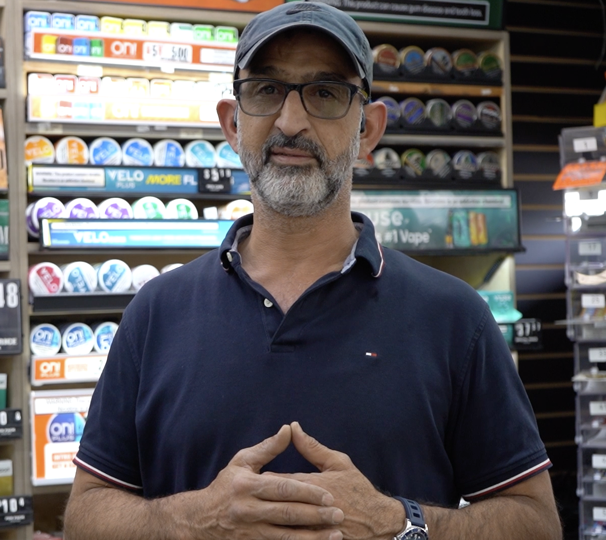 Man in a convenience store standing in front of shelves of nicotine pouches and vape products
