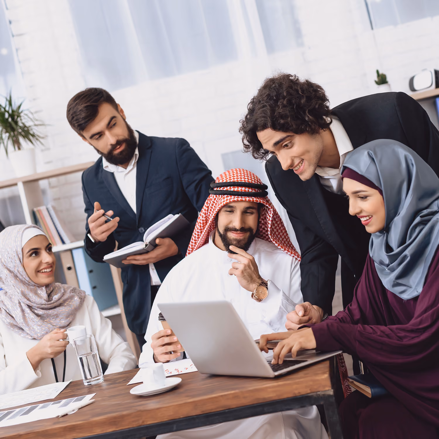 Group of diverse professionals collaborating around a laptop in a modern office setting.