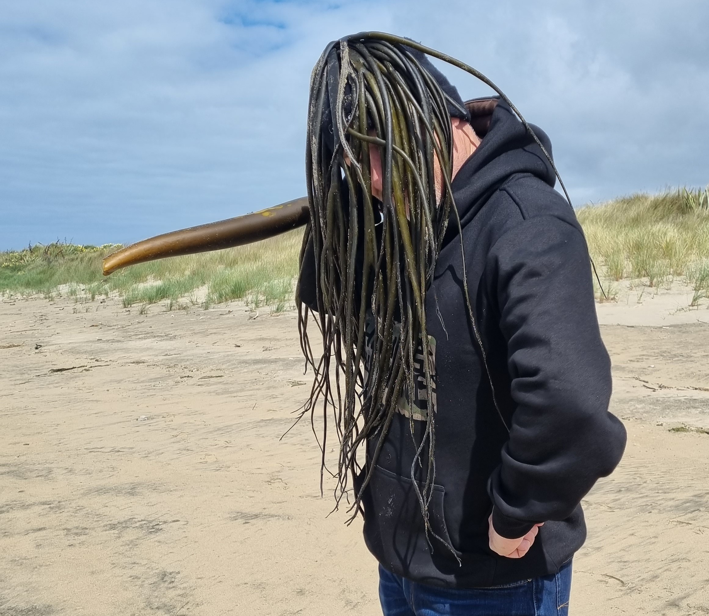 Wayne standing on a beach with seaweed over his head
