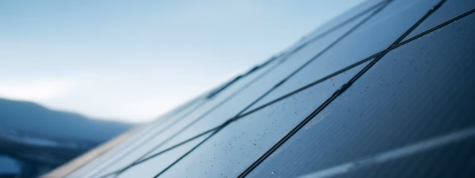 Close-up view of solar panels angled against a clear sky with mountains in the background.