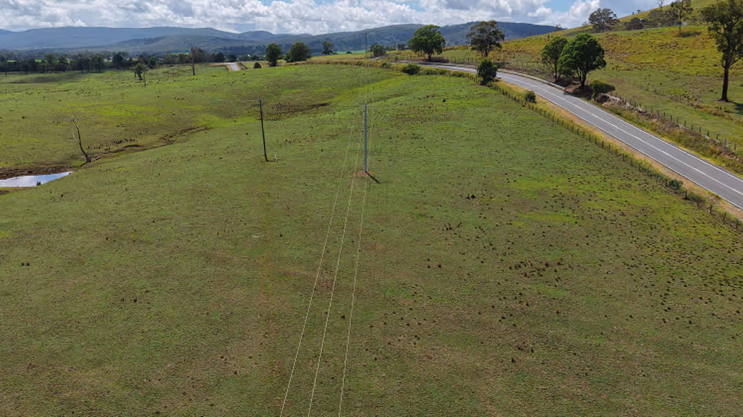 Open green paddock with a rural energy site in the background under a clear sky.