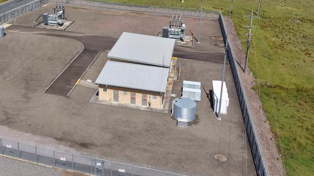 Aerial view of a rural electrical substation with a control building and surrounding gravel yard.