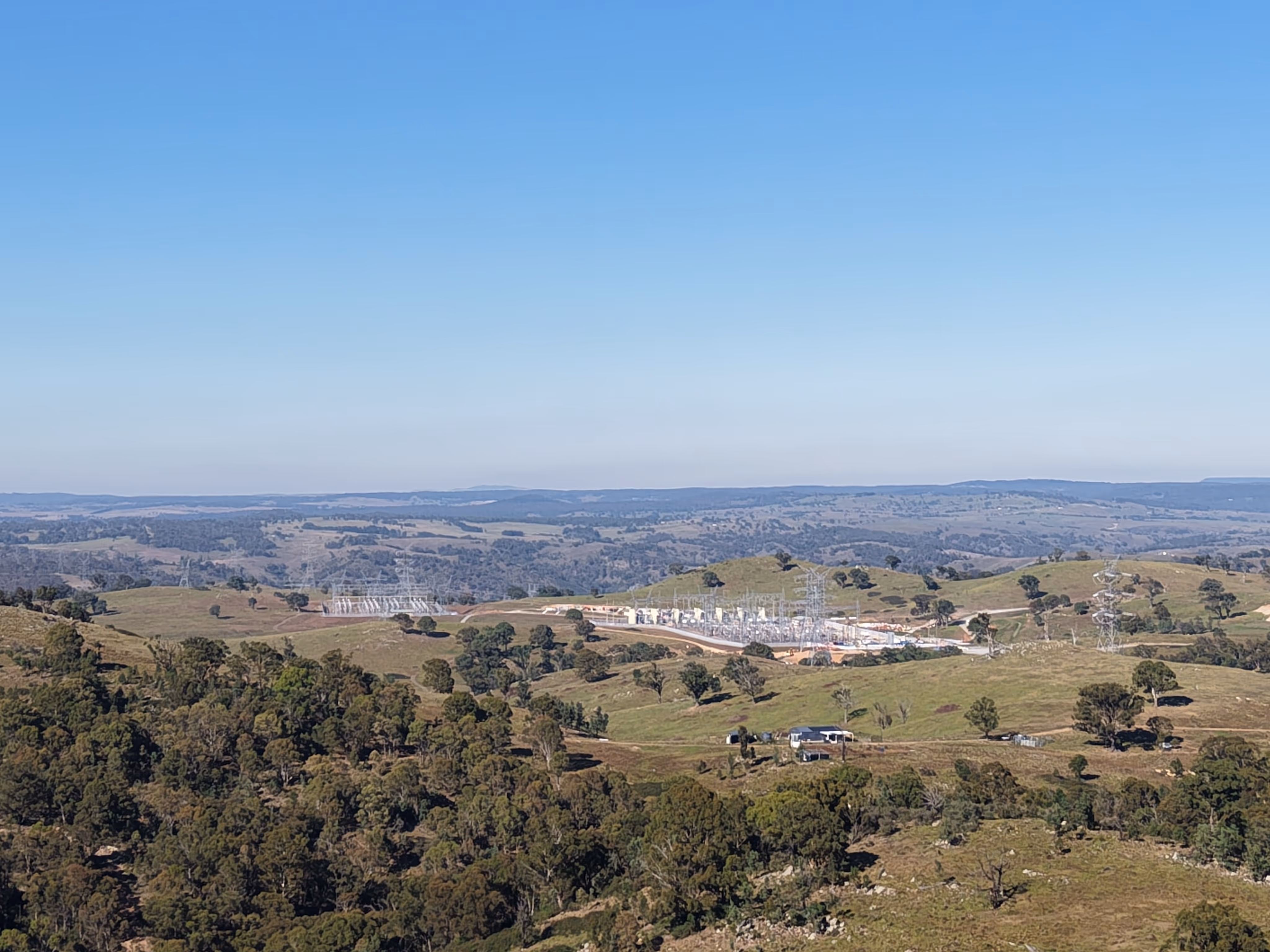 Electrical substation situated among green rolling hills under a clear blue sky.