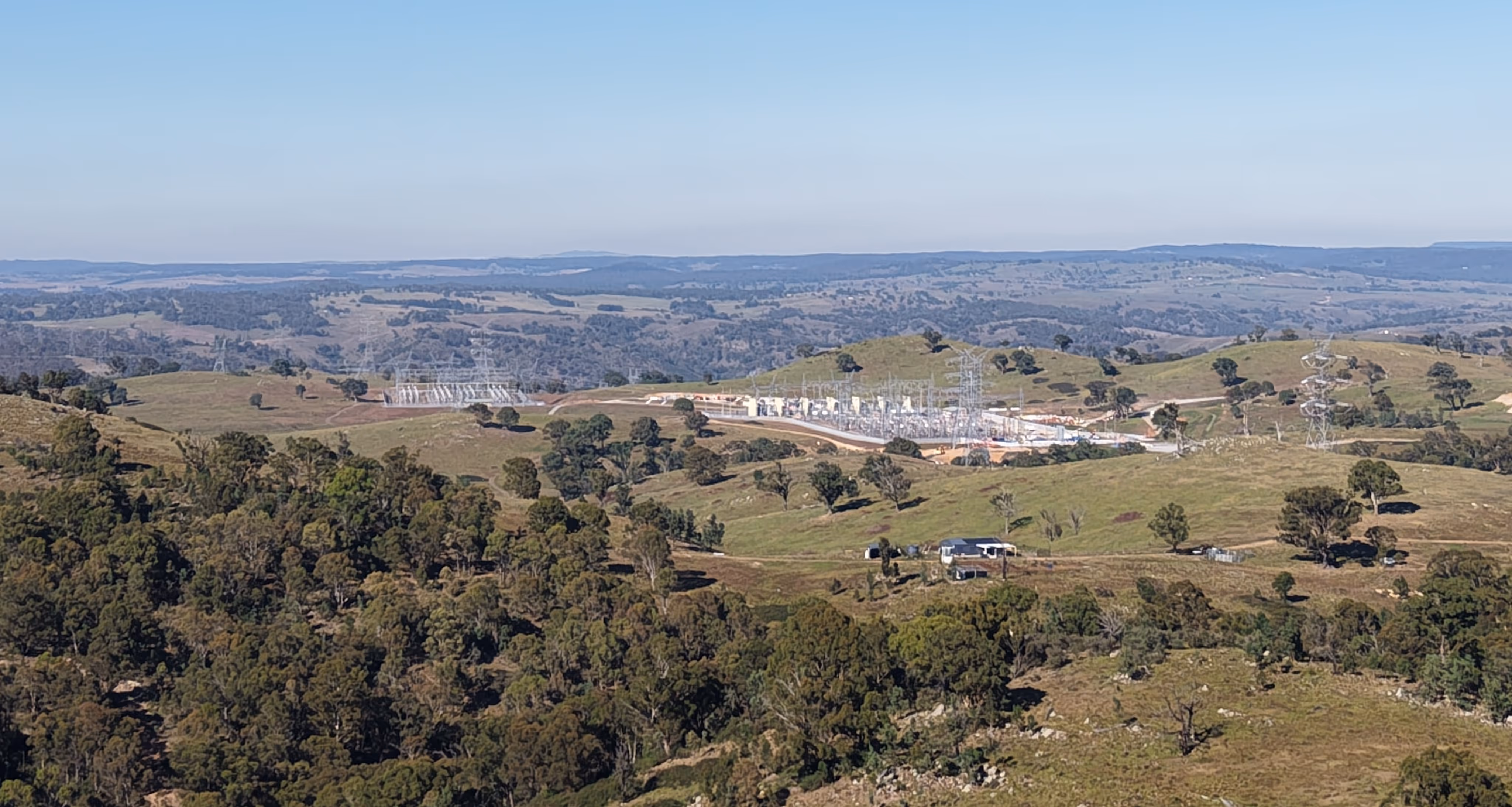 Electrical substation situated among green rolling hills under a clear blue sky.