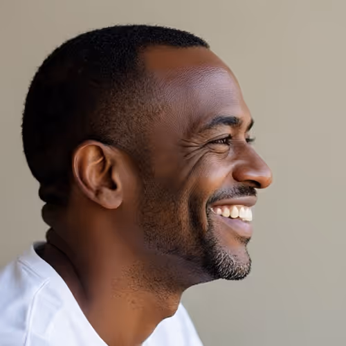 Profile of a smiling African American man with short hair and a beard wearing a white shirt against a gray background.