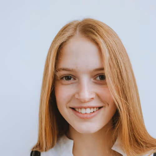 Young woman with long red hair smiling against a plain light background.
