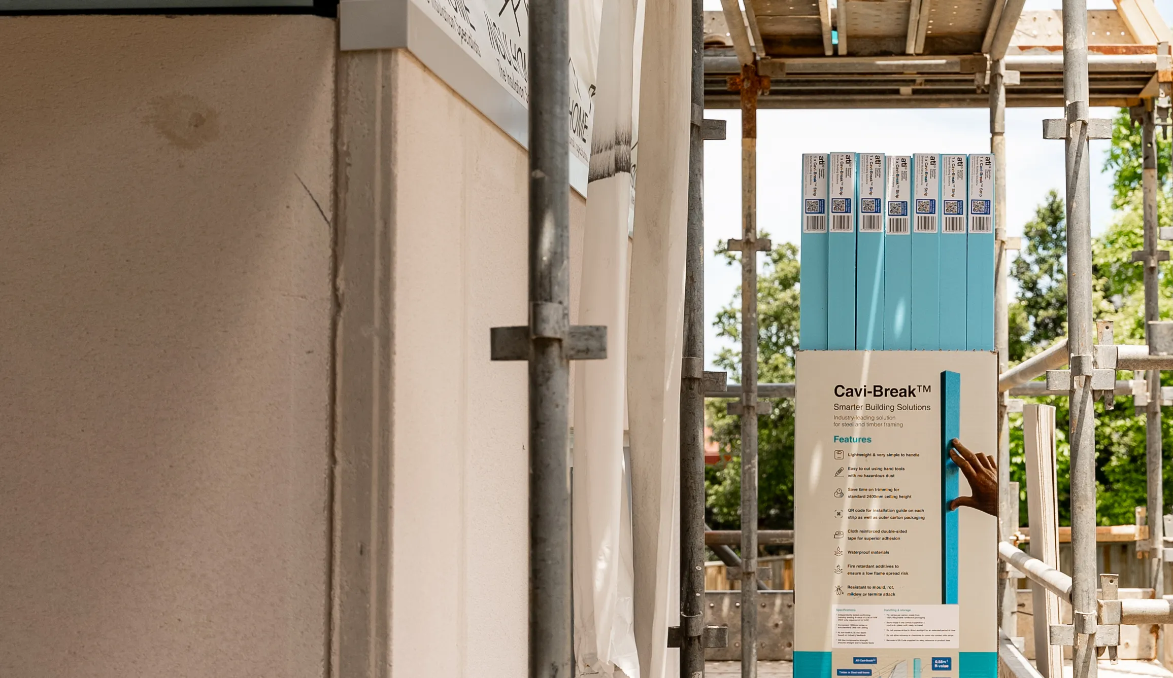 Stacks of Cavi-Break insulation panels on a construction site with scaffolding and a worker's hand holding one panel.