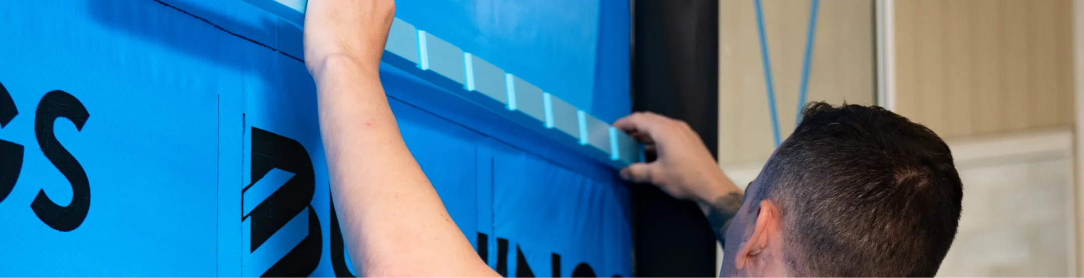 Person with dark hair installing blue insulation material on a wall indoors.