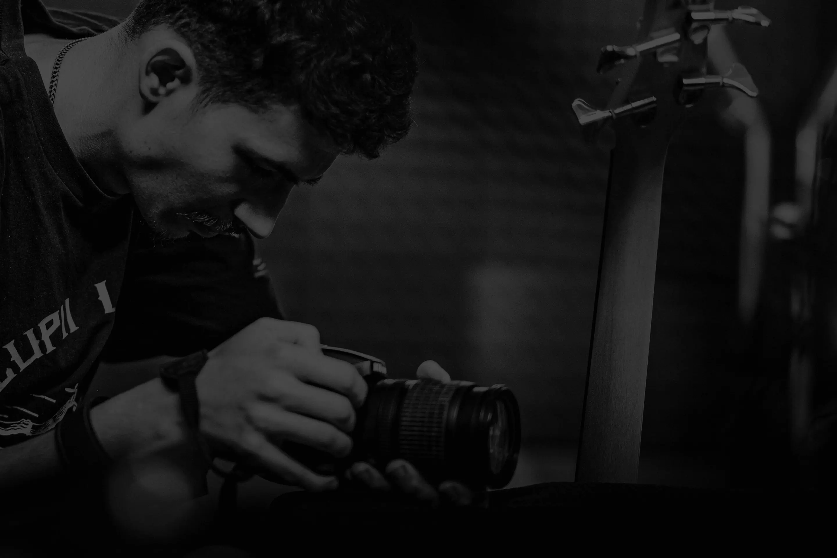 Man examining a camera in a low-lit room with a guitar neck in the background.