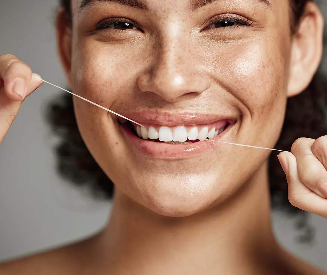 Close-up of a smiling woman flossing her teeth with dental floss.