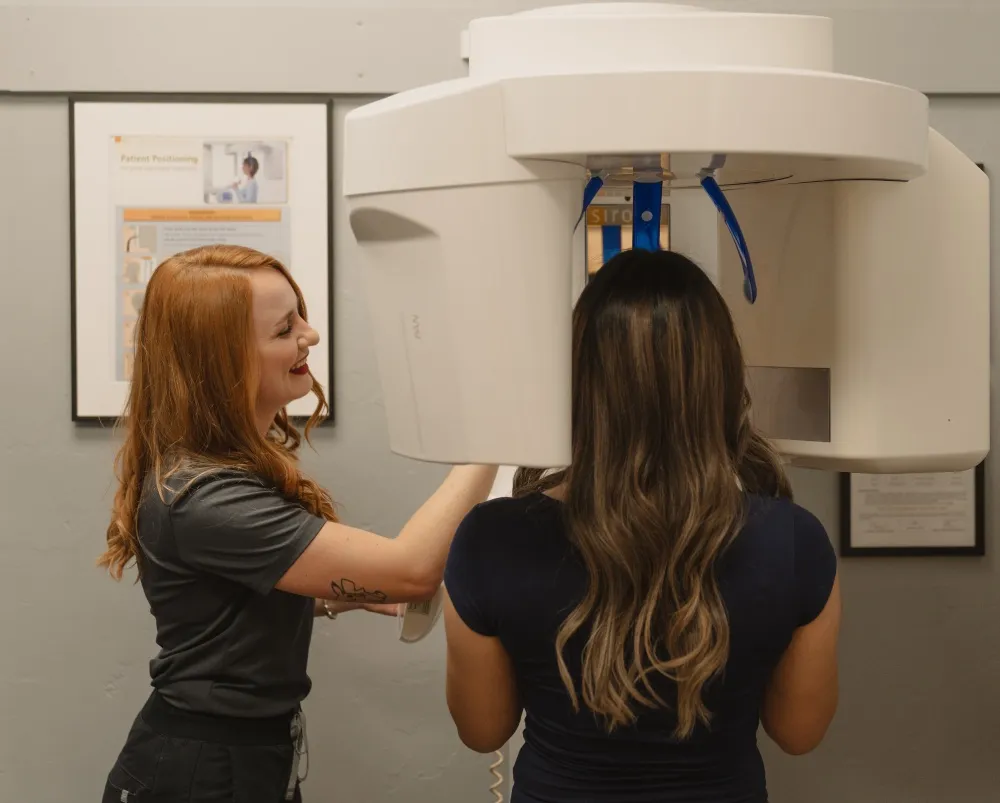 Dental technician assisting a patient standing in a panoramic dental X-ray machine.