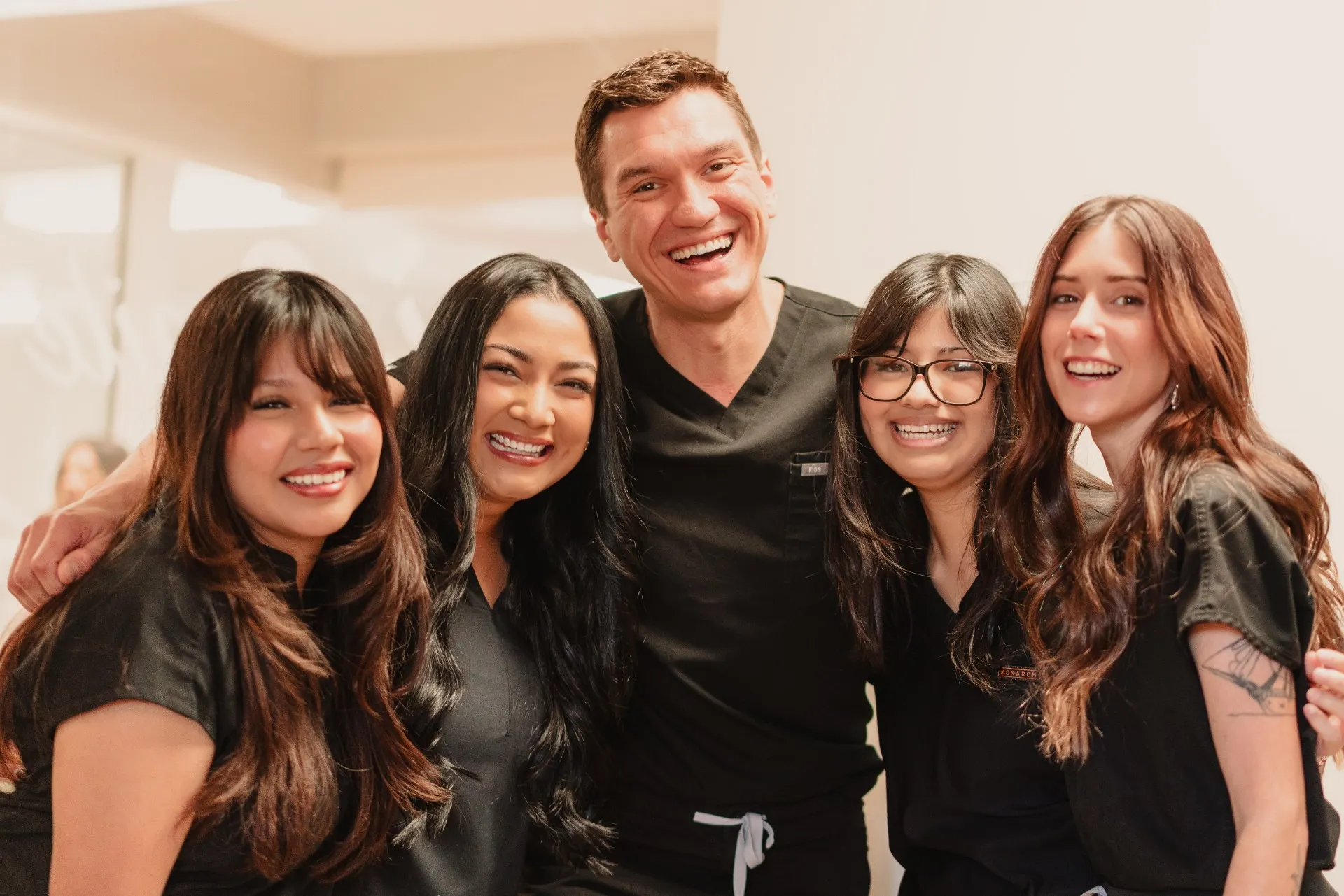 Group of five smiling healthcare professionals wearing black scrubs posing together indoors.
