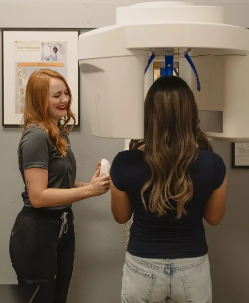 Dental professional assisting a patient with a panoramic dental X-ray machine.