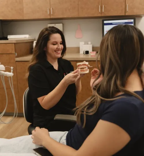 Dental professional showing a dental model to a patient seated in a dental chair.