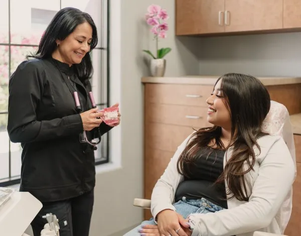 Dentist showing a dental model to a smiling female patient seated in a dental office chair.