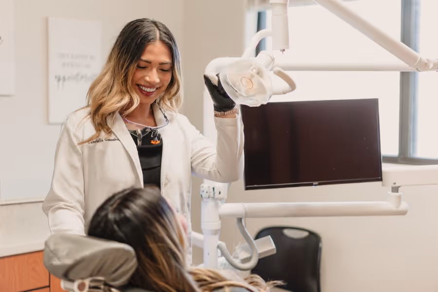 Female dentist smiling and adjusting dental light while patient reclines in chair at clinic.