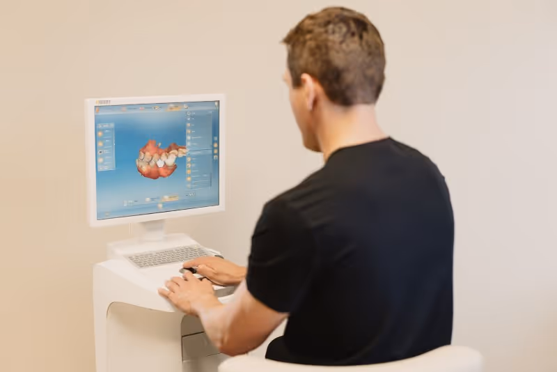 Man in black shirt using dental software showing 3D model of teeth on a computer screen.