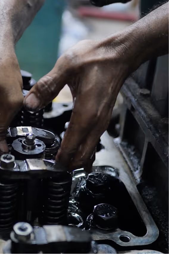 Mands hænder arbejder på en motor med synlige metaldele og fjederkomponenter.