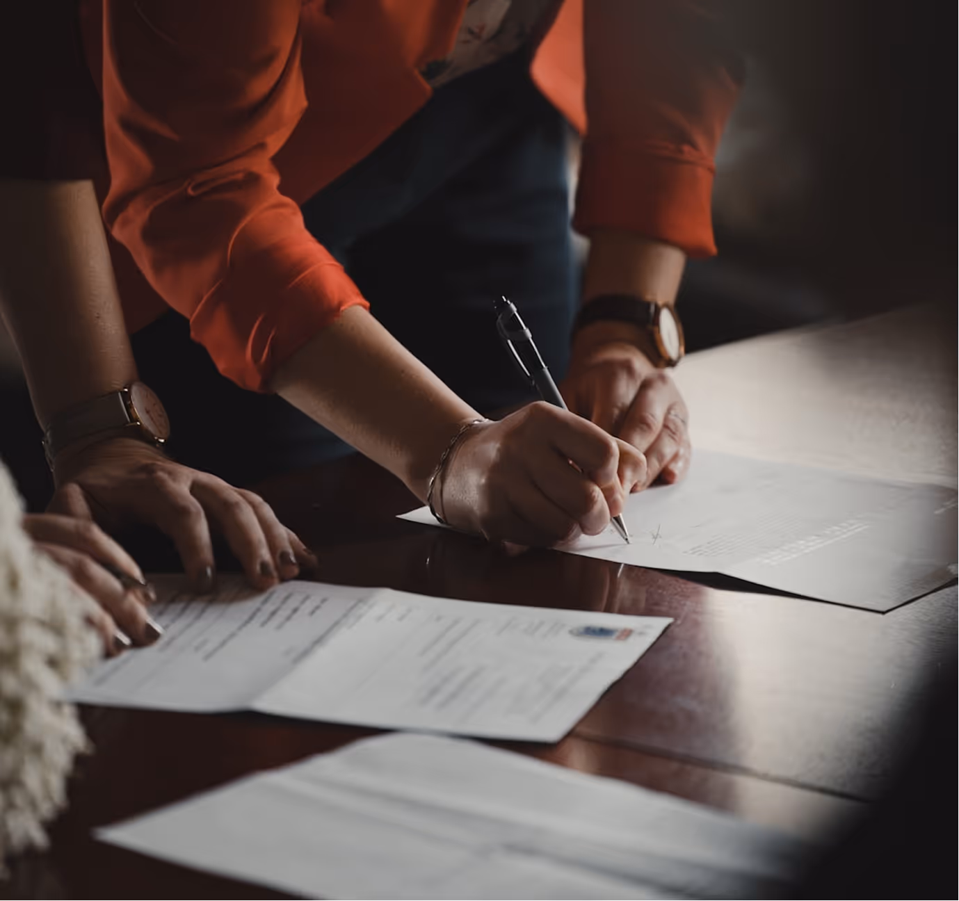 Two people are signing documents at a table, with one of them holding a pen and writing.