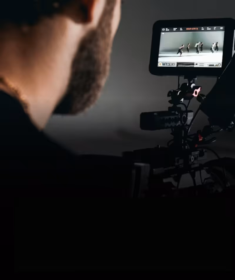 Close-up of a man with a beard filming dancers performing a routine on a camera monitor.