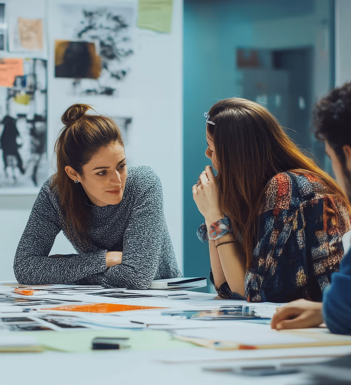 Three young adults collaborating over papers and documents on a table in a modern office setting.