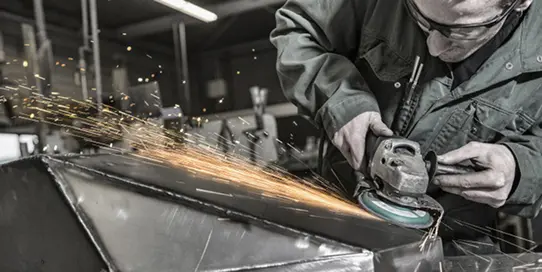 Worker wearing safety glasses grinding metal with an angle grinder, sparks flying.