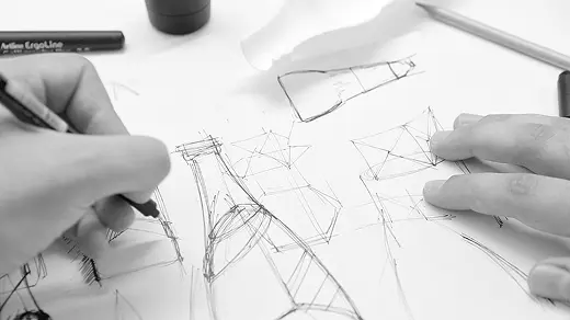 Hands sketching architectural or design drawings with pen on white paper.