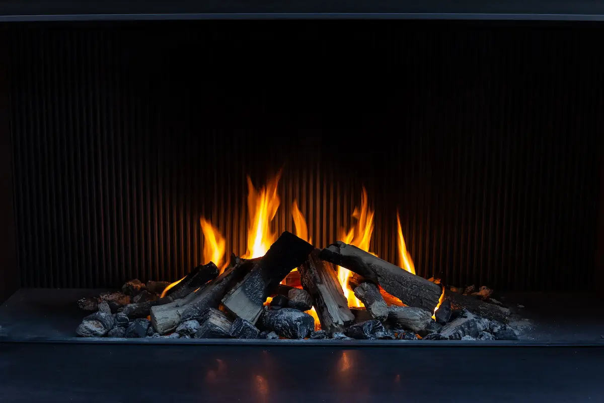 Bright orange flames burning on blackened logs in a modern indoor fireplace.