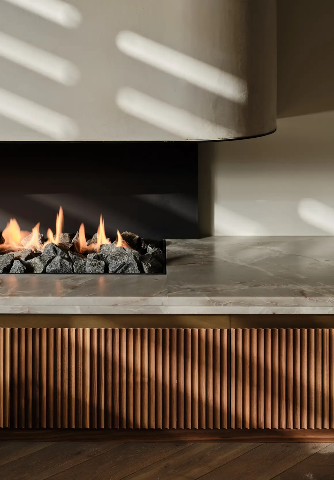 Modern fireplace with flames over grey stones, marble mantel, and vertical wood paneling below.