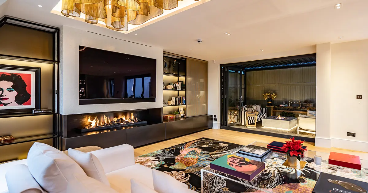 Modern living room with white sofa, colorful rug, fireplace, TV, and open view to outdoor seating area.
