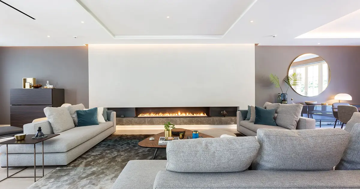 Modern living room with gray sofas, a long fireplace, round mirror, and decorative plants.