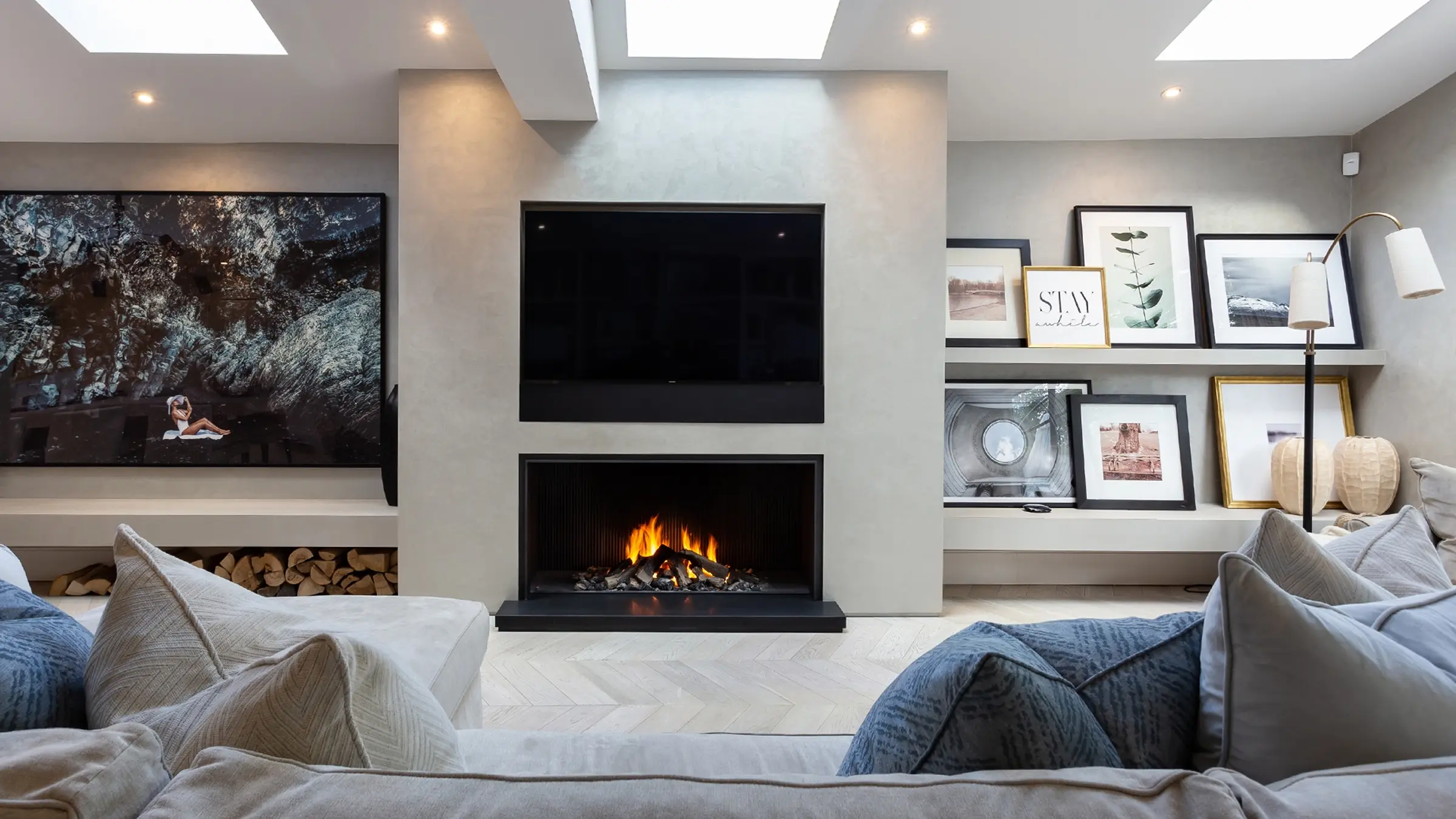 Modern living room with a fireplace, TV above it, large sofa, and framed art on shelves.