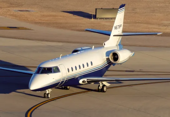 White private jet with blue stripes taxiing on airport runway in daylight.