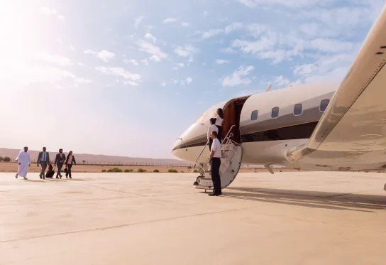 People walking toward a private jet with staff standing 