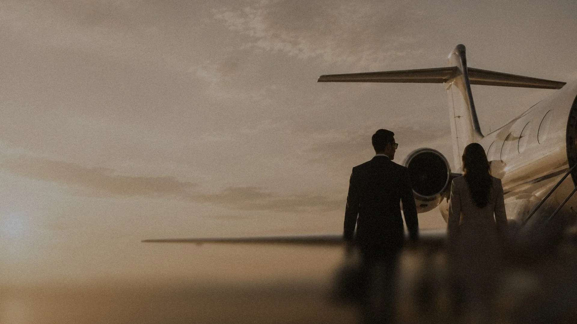 Silhouettes of a man and woman walking towards a private jet during sunset.