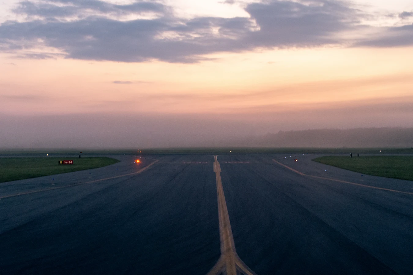 Runway at an airport during dusk with fog and a colorful sky in the background.
