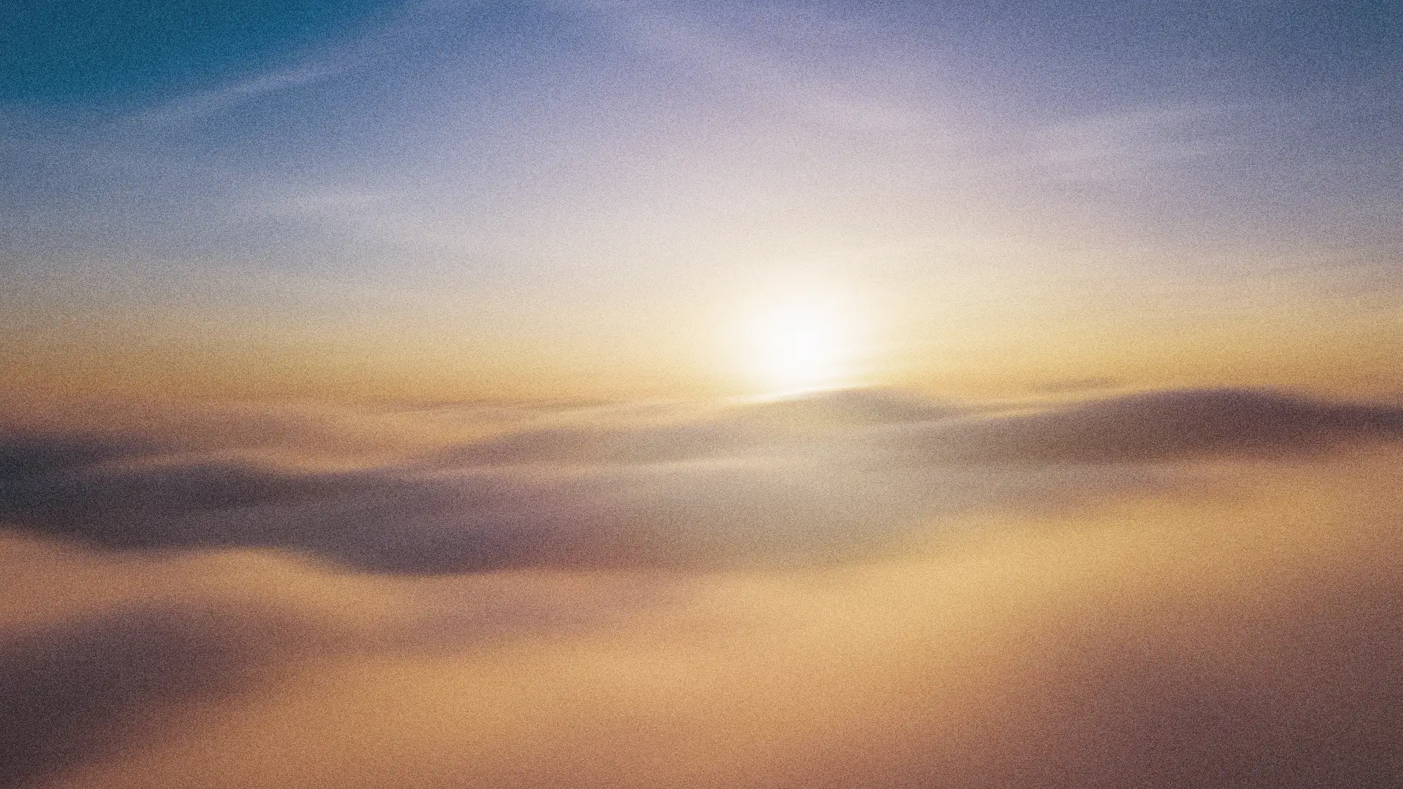 Sun rising or setting above soft clouds with a clear blue sky.