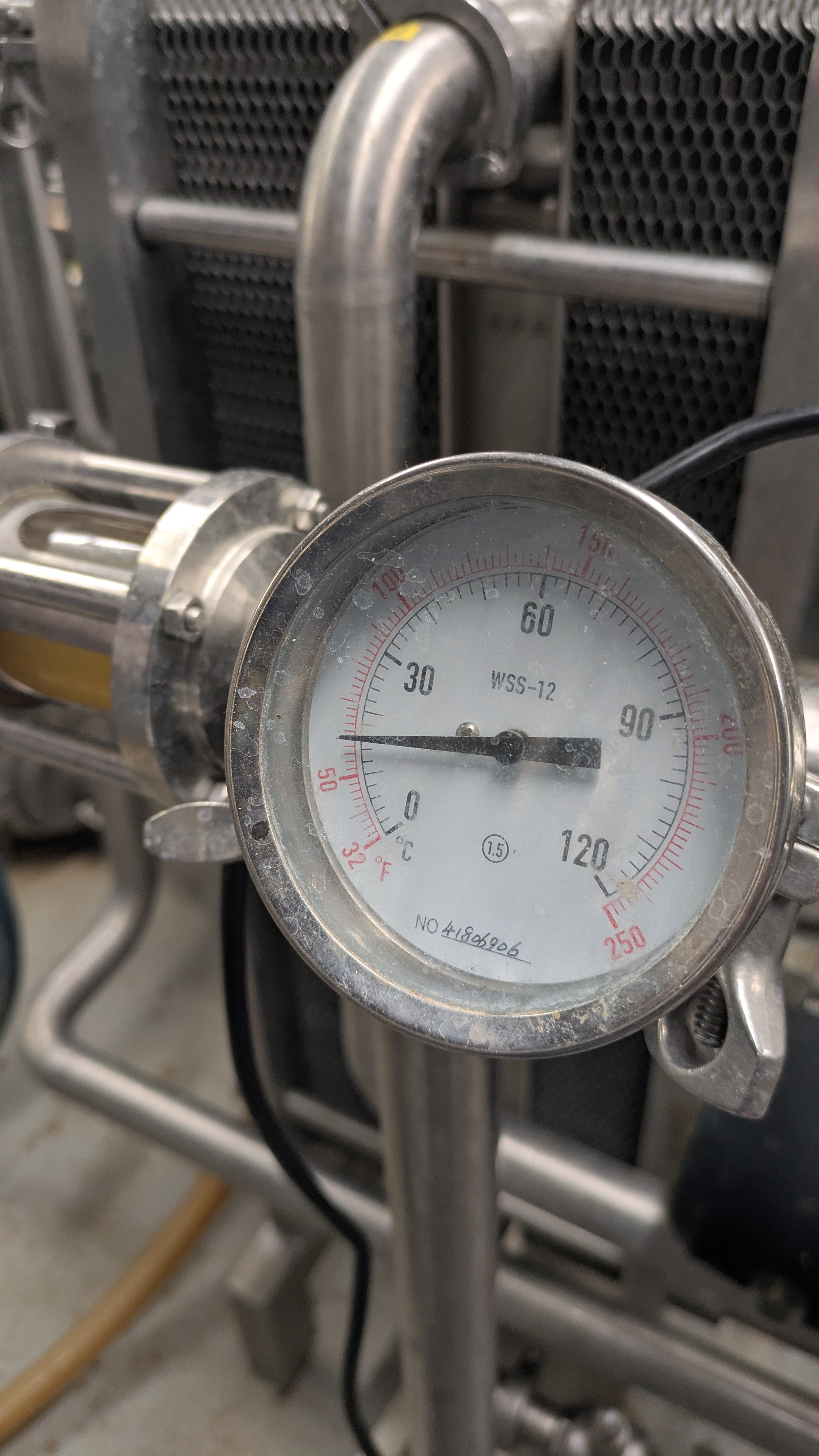 Round analog pressure gauge on metal pipe with temperature scales in Celsius and Fahrenheit.