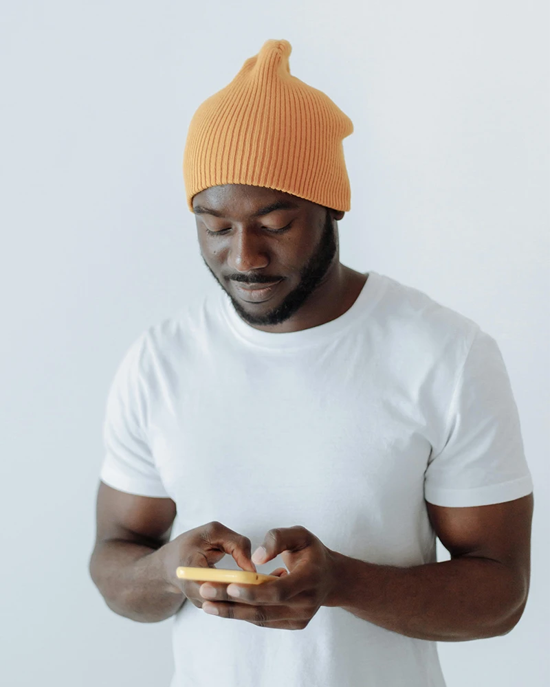 Man wearing orange knit hat and white t-shirt looking down at yellow smartphone in his hands.