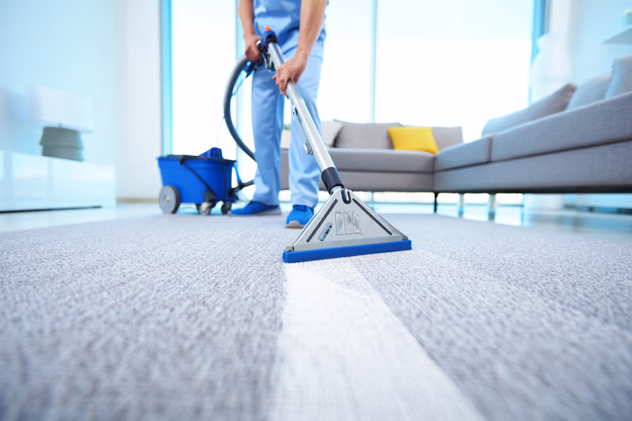 Professionnel nettoyant un tapis gris avec une machine dans un salon lumineux moderne.