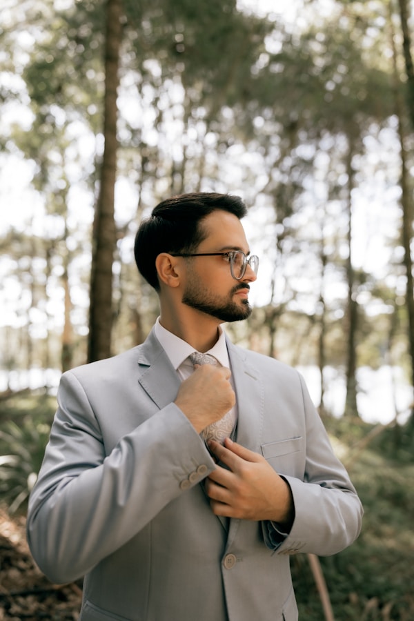 Man in a light grey suit adjusting his tie outdoors.