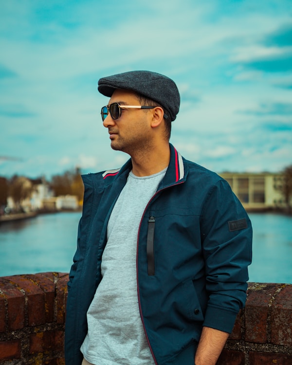 Man wearing a flat cap and sunglasses by water