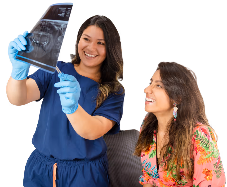 Dentist in blue scrubs holding a dental X-ray and explaining it to a smiling female patient in a colorful floral shirt.