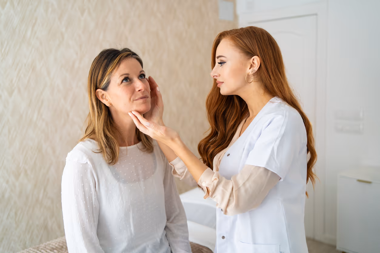 Female healthcare professional examining a woman's face in a clinical setting.