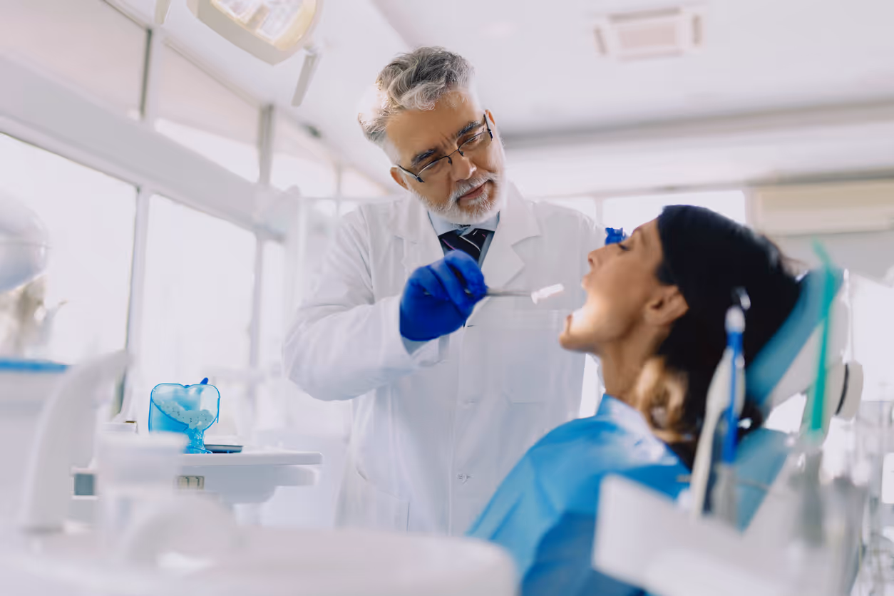 Dentist in white coat explaining dental implants using tooth models to a female patient.