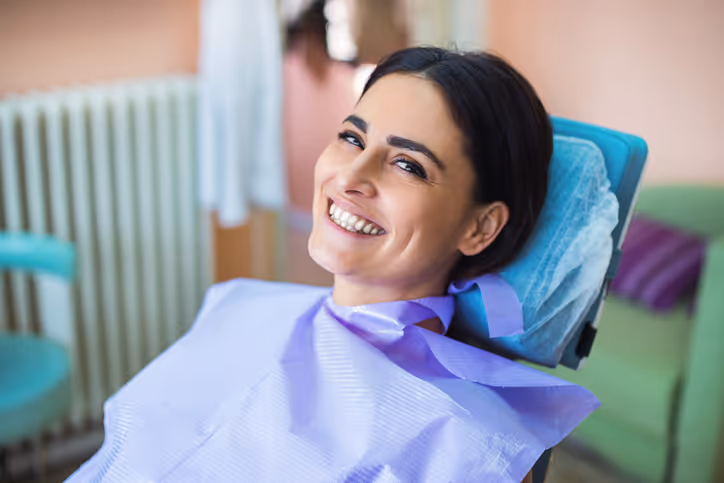 Smiling woman reclining in a dental chair with a purple dental bib.
