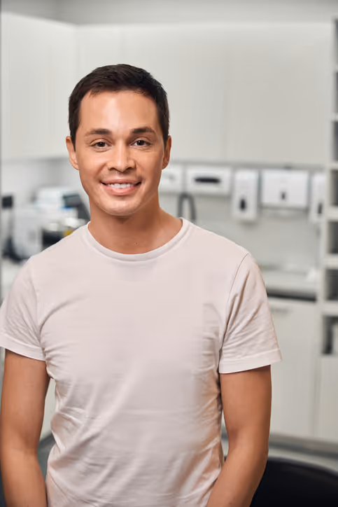 Smiling young man wearing a light-colored t-shirt standing in a modern dental office.