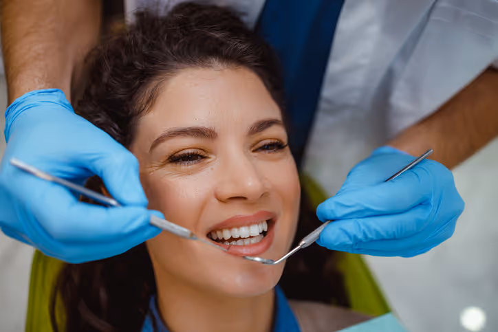 Smiling woman receiving dental check-up with tools held by gloved hands.