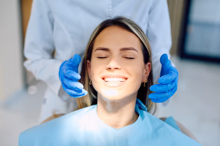 Smiling woman in a dental chair with a dentist wearing blue gloves behind her.